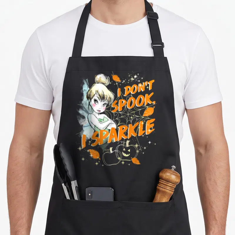 Peter halloween apron - Cartoon fairy with blue wings next to orange text I DON T SPOOK I SPARKLE on spiderweb — shown on a black cotton canvas apron against a white background