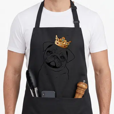 Miller dog apron - Black line art pug head with realistic gold crown featuring blue and red gems — shown on a black cotton canvas apron against a white background