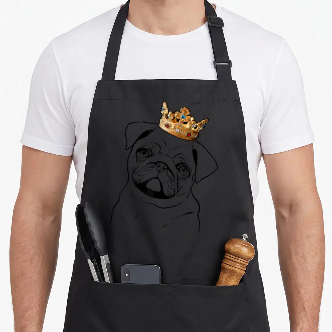 Miller dog apron - Black line art pug head with realistic gold crown featuring blue and red gems — shown on a black cotton canvas apron against a white background