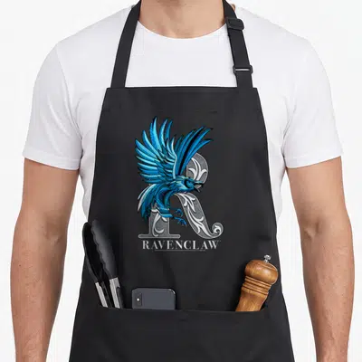 Mosaic eagles grill apron - Blue raven perched on ornate grey R with Ravenclaw text below — shown on a black cotton canvas apron against a white background
