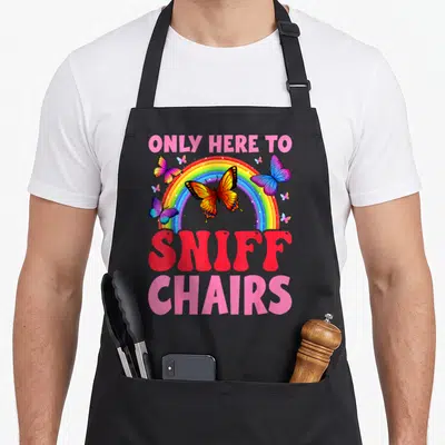 Embarrassing inappropriate apron - Rainbow with butterflies and text ONLY HERE TO SNIFF CHAIRS in pink and red — shown on a black cotton canvas apron against a white background