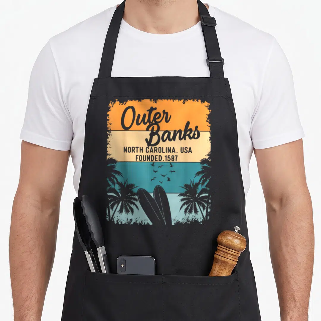 Obx outer banks apron - Retro striped graphic with Outer Banks text, surfboards, palm trees, and birds in orange teal — shown on a black cotton canvas apron against a white background