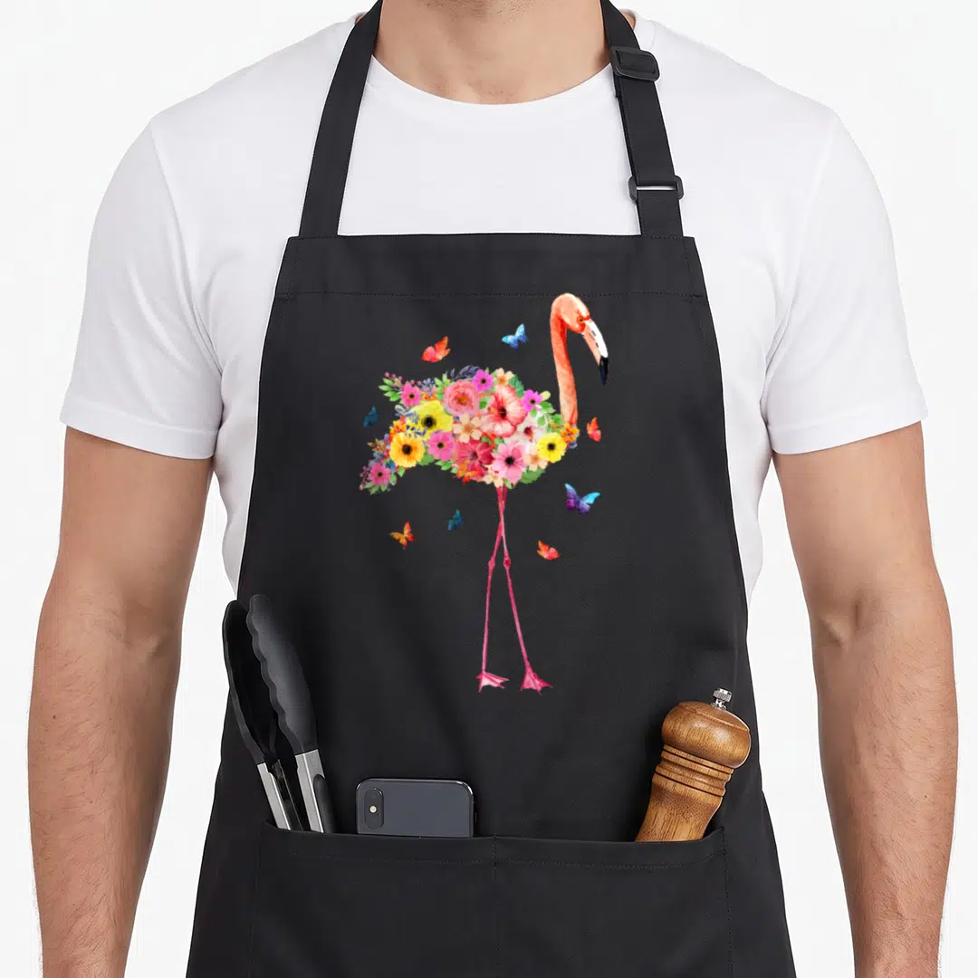 Hawaiian pink flamingo apron - Watercolor flamingo body made of pink yellow and blue flowers with butterflies — shown on a black cotton canvas apron against a white background