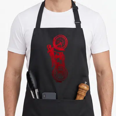 Funny motorcycle biker apron - Vertical red line-art drawing of a vintage motorcycle showing engine and spoked wheels — shown on a black cotton canvas apron against a white background