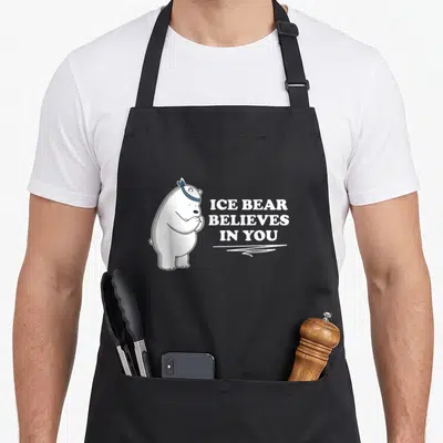 Ice bear apron - Polar bear cartoon with blue bandana and believes in you text — shown on a black cotton canvas apron against a white background