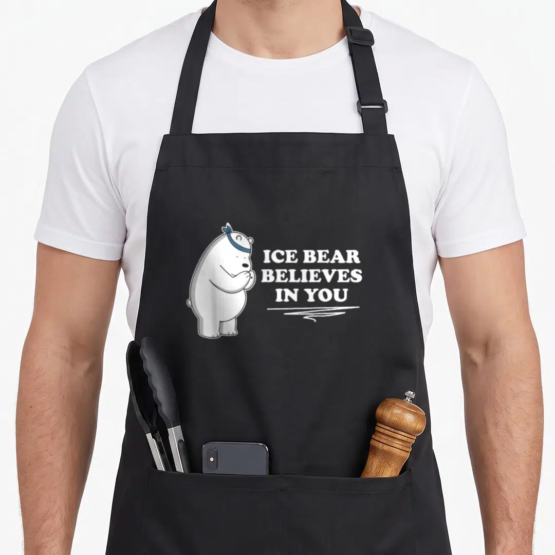 Ice bear apron - Polar bear cartoon with blue bandana and believes in you text — shown on a black cotton canvas apron against a white background