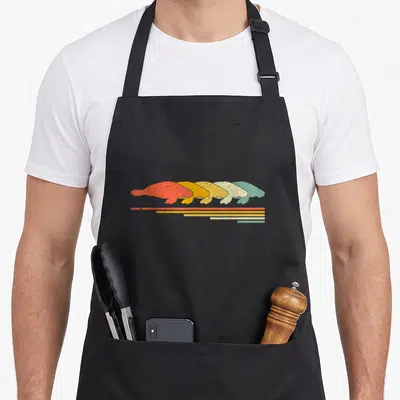 Manatee 70s apron - Five overlapping manatees in red orange yellow green teal facing left above matching horizontal — shown on a black cotton canvas apron against a white background