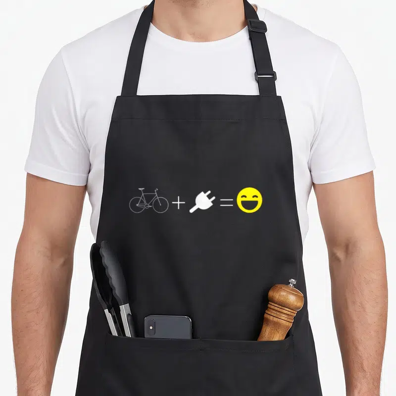 Equation bike apron - White bicycle icon plus white plug equals yellow smiley face on grey background — shown on a black cotton canvas apron against a white background