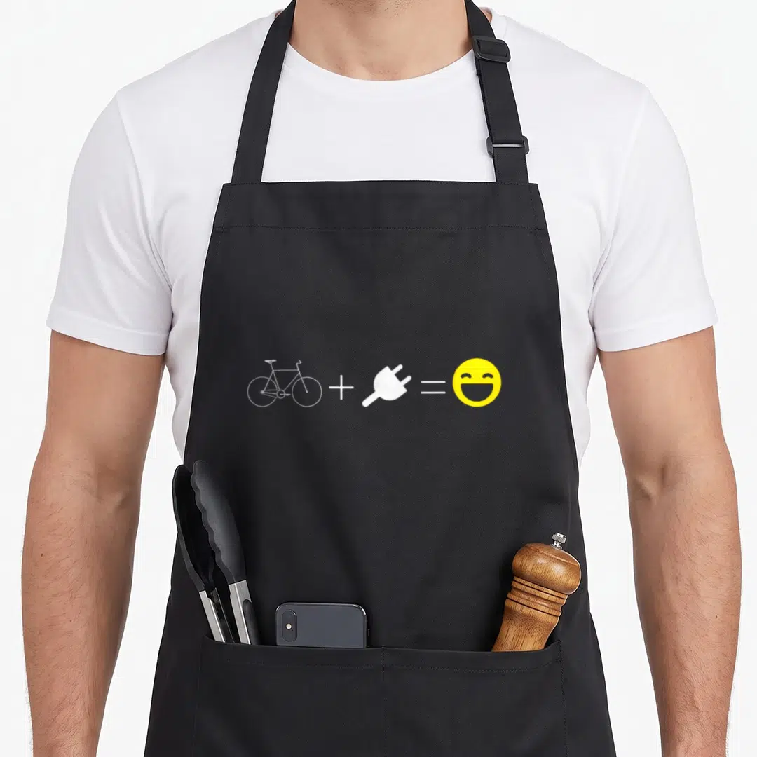 Equation bike apron - White bicycle icon plus white plug equals yellow smiley face on grey background — shown on a black cotton canvas apron against a white background