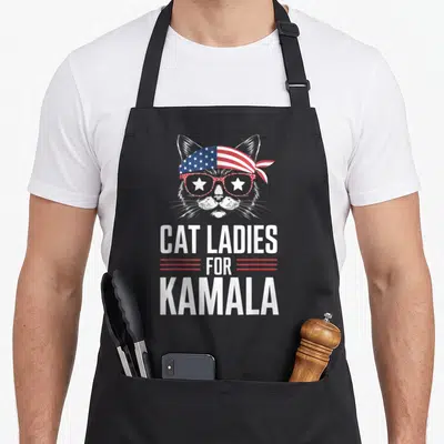 Kamala cat lady apron - Realistic cat head wearing stars and stripes bandana and glasses above stacked text CAT LADIES — shown on a black cotton canvas apron against a white background