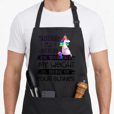 Weight business apron - Cartoon unicorn with rainbow mane next to stacked text about weight privacy — shown on a black cotton canvas apron against a white background
