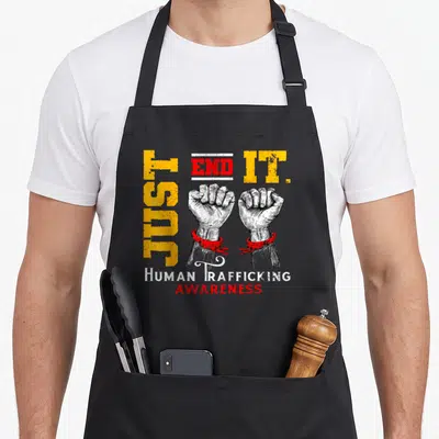 End modern apron - Two white fists in red handcuffs with vertical Just End It text — shown on a black cotton canvas apron against a white background