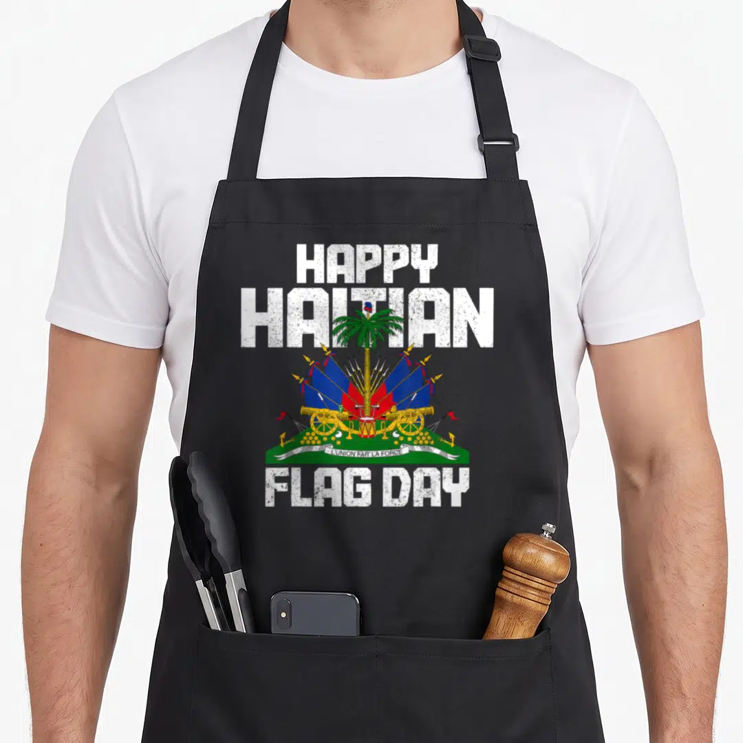 Flag haiti pride apron - HAPPY HAITIAN FLAG DAY text framing Haitian coat of arms with palm tree, flags, cannons — shown on a black cotton canvas apron against a white background