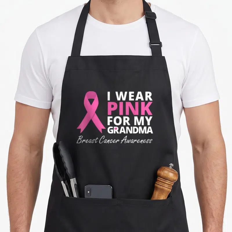 Ribbon grandma apron - Pink awareness ribbon next to stacked text reading I Wear Pink For My Grandma Breast Cancer — shown on a black cotton canvas apron against a white background
