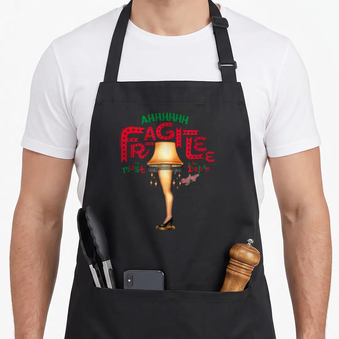 Ahh christmas apron - Leg lamp graphic with arched AHHHHHHH and red Fragilee text in cartoon style — shown on a black cotton canvas apron against a white background