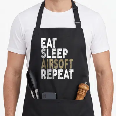 Sleep airsoft apron - Stacked EAT SLEEP AIRSOFT REPEAT text in white and tan distressed typography — shown on a black cotton canvas apron against a white background