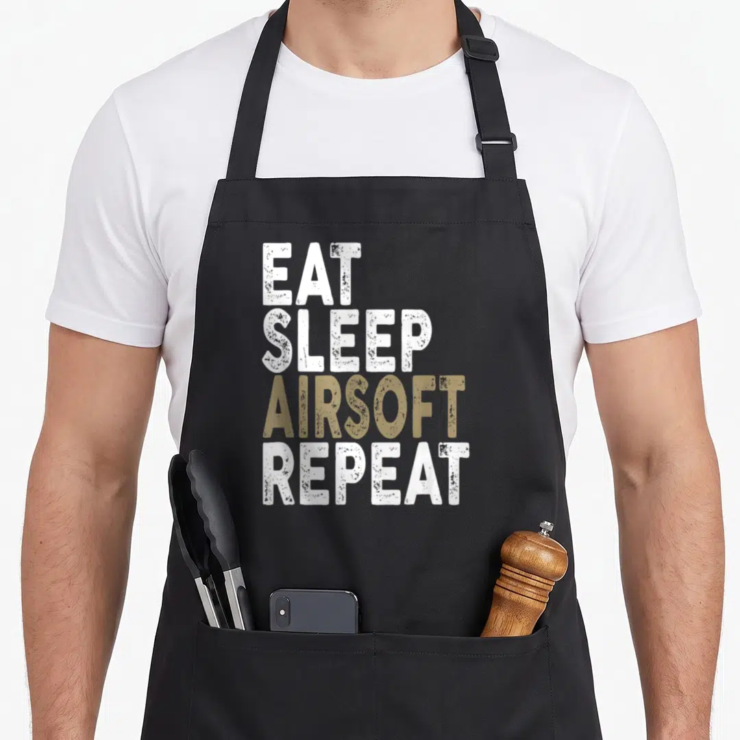 Sleep airsoft apron - Stacked EAT SLEEP AIRSOFT REPEAT text in white and tan distressed typography — shown on a black cotton canvas apron against a white background