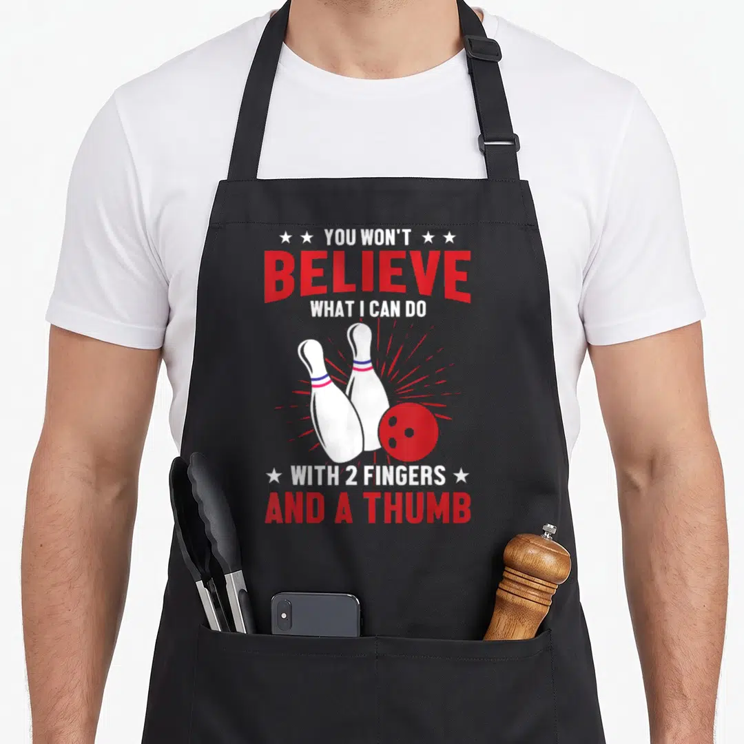 Bowler bowling green apron - Red and white text and bowling pins with ball and action lines — shown on a black cotton canvas apron against a white background