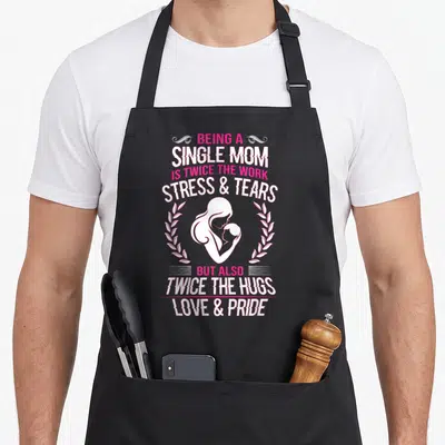 Stress single mom apron - Pink and white stacked text surrounding a mother and child silhouette inside a laurel wreath — shown on a black cotton canvas apron against a white background