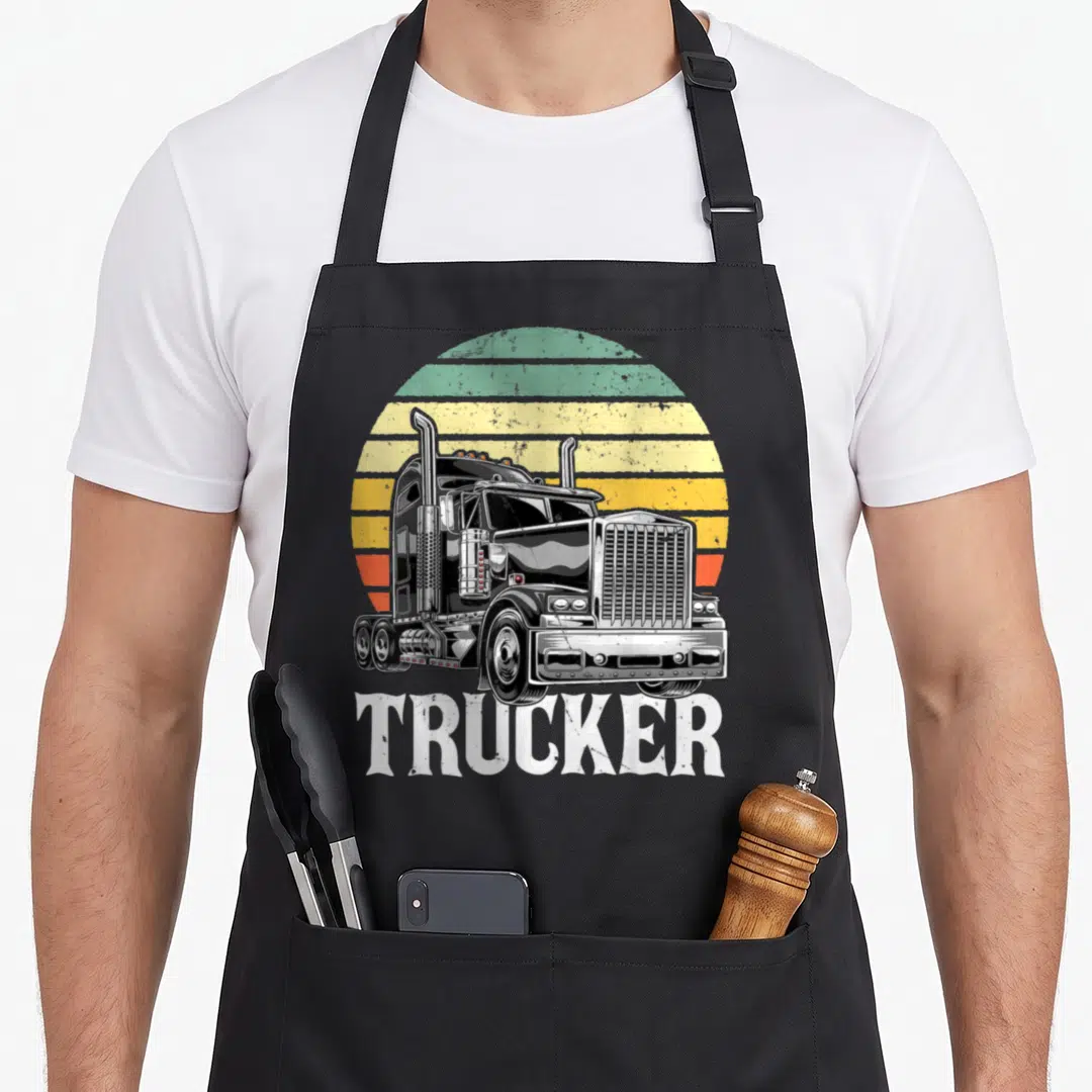 Trailer driver semi truck apron - Retro semi-truck illustration with striped sun and TRUCKER text in black white yellow — shown on a black cotton canvas apron against a white background