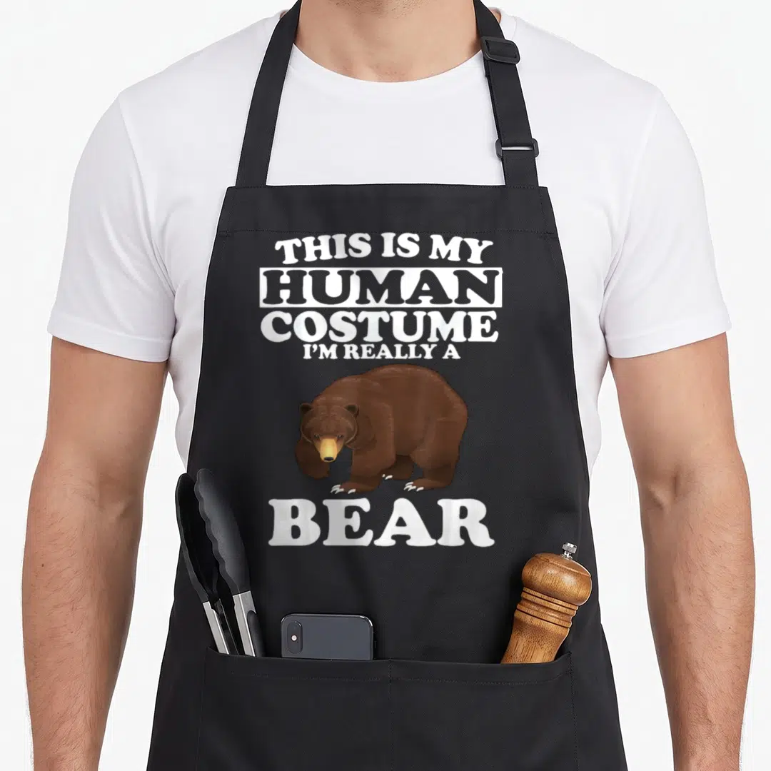 Costume bear halloween apron - This Is My Human Costume I'm Really a Bear text above and below brown bear — shown on a black cotton canvas apron against a white background