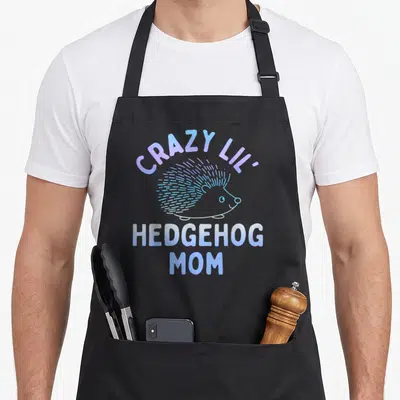 Lil mother's day aprons - Purple and blue text CRAZY LIL HEDGEHOG MOM above cartoon hedgehog on black fabric — shown on a black cotton canvas apron against a white background