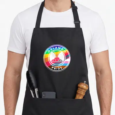 Orlando pride apron - Circular rainbow logo with white fountain silhouette and ORLANDO PRIDE text in black border — shown on a black cotton canvas apron against a white background