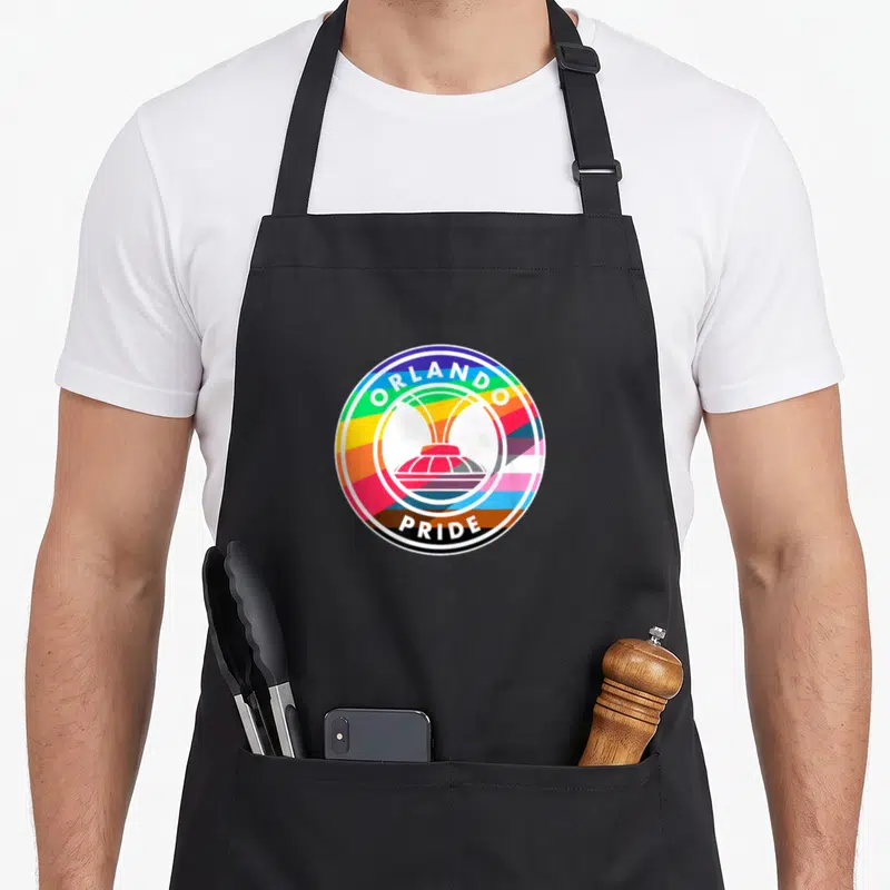 Orlando pride apron - Circular rainbow logo with white fountain silhouette and ORLANDO PRIDE text in black border — shown on a black cotton canvas apron against a white background