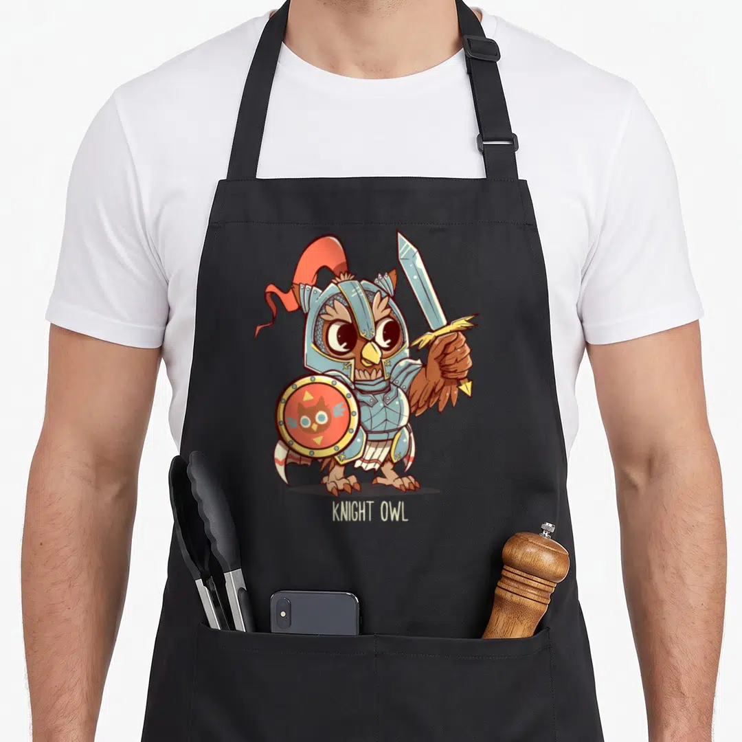 Knight owl apron - Cartoon owl in silver armor holding sword and red shield with text below — shown on a black cotton canvas apron against a white background