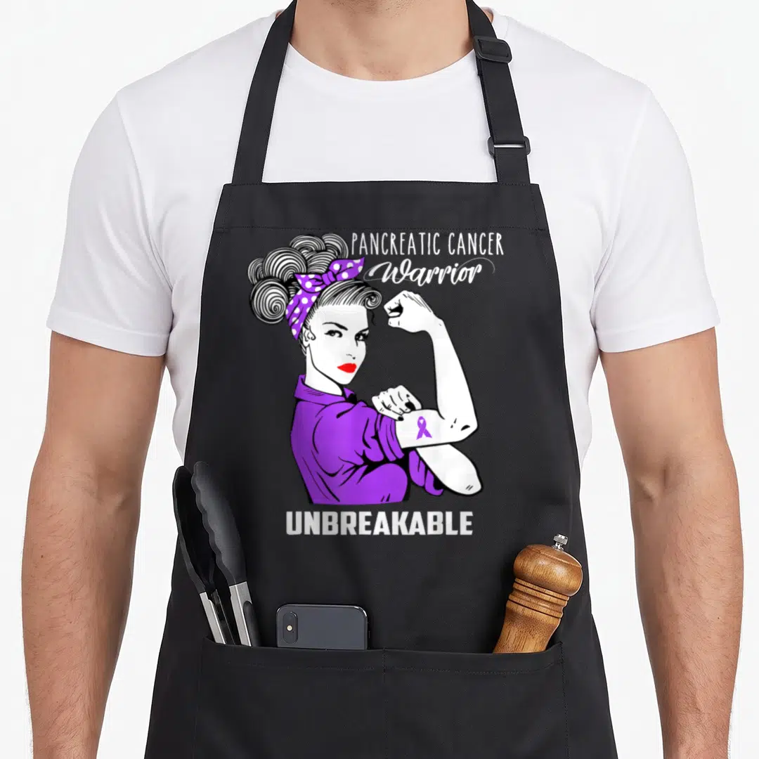 Pancreatic cancer awareness apron - Cartoon woman flexing purple ribbon with PANCREATIC CANCER Warrior UNBREAKABLE text — shown on a black cotton canvas apron against a white background