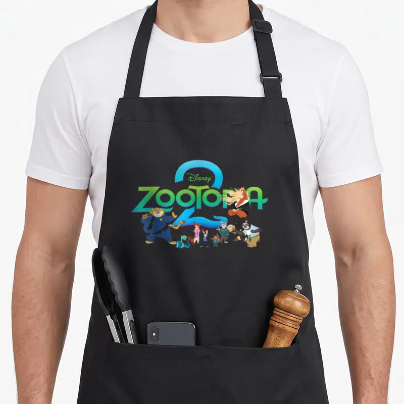 Illustrated character aprons - Zootopia characters standing in front of green Disney logo text inside a blue arch — shown on a black cotton canvas apron against a white background
