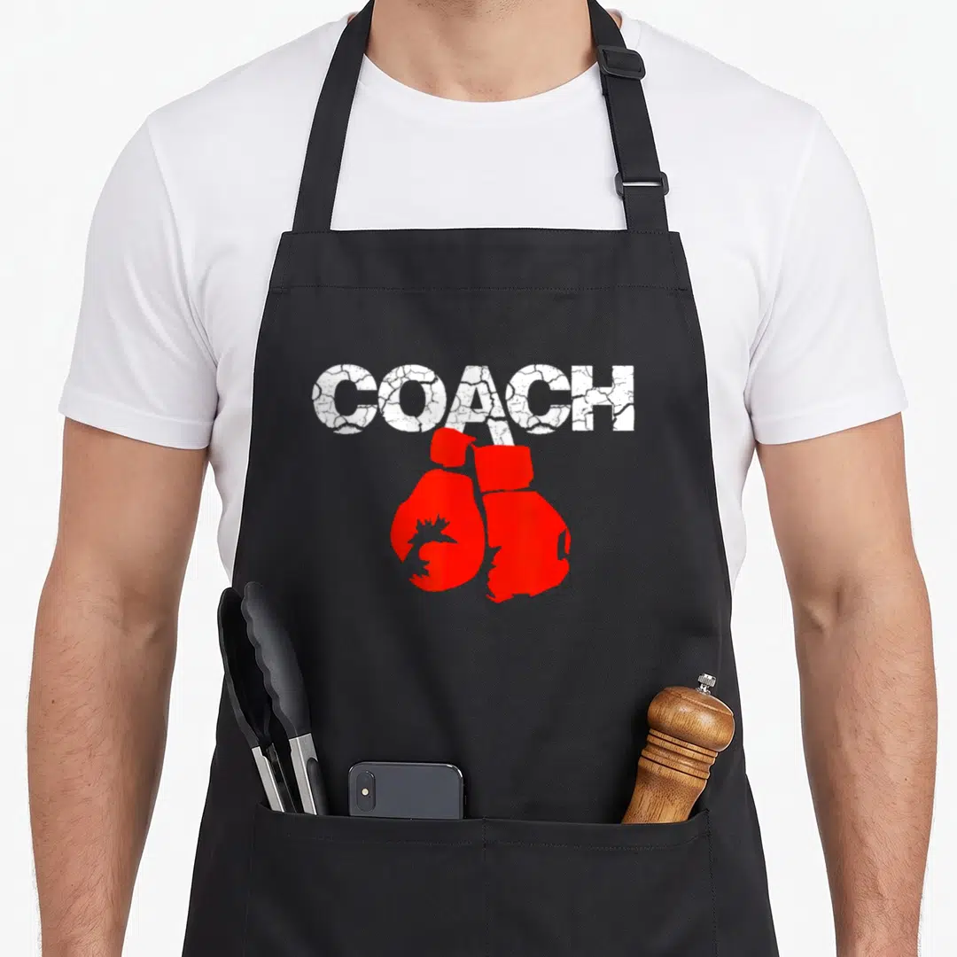 Definition boxing coach apron - Distressed white COACH text above a pair of red boxing gloves — shown on a black cotton canvas apron against a white background