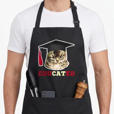 Educated cat apron - Tabby cat head in black graduation cap with red tassel above red and yellow EDUCATED text — shown on a black cotton canvas apron against a white background