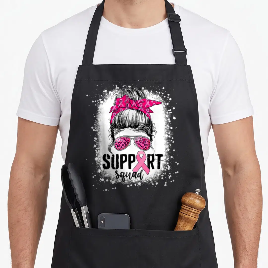 Support messy aprons - Woman bun leopard sunglasses pink ribbon SUPPORT squad white splatter — shown on a black cotton canvas apron against a white background