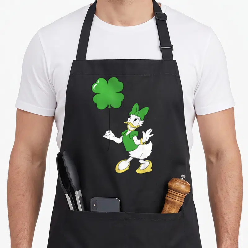 Leaf daisy apron - Cartoon Daisy Duck holding green four-leaf clover balloon wearing green outfit and yellow shoes — shown on a black cotton canvas apron against a white background