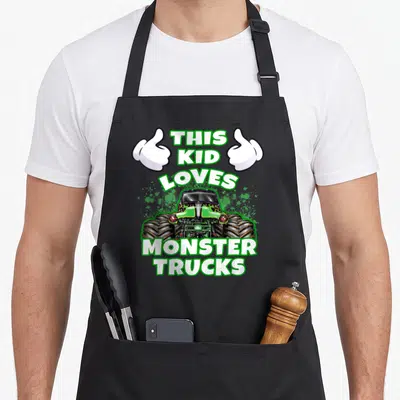 Cute monster truck aprons - This Kid Loves Monster Trucks text with green truck and two thumbs up hands on black apron — shown on a black cotton canvas apron against a white background