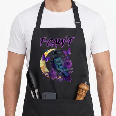 Caw raven halloween apron - F-CAW-F text above a crow perched on purple roses and blue butterflies against a yellow — shown on a black cotton canvas apron against a white background