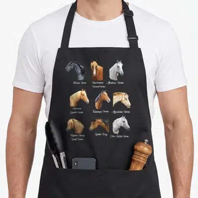 Breed horse apron - Nine cartoon horse heads in a grid with breed names like Friesian and Appaloosa printed in script — shown on a black cotton canvas apron against a white background