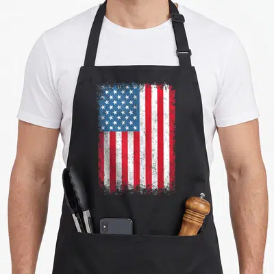 Patriotic flag 4th of july apron - Distressed red white and blue USA flag print on black fabric — shown on a black cotton canvas apron against a white background