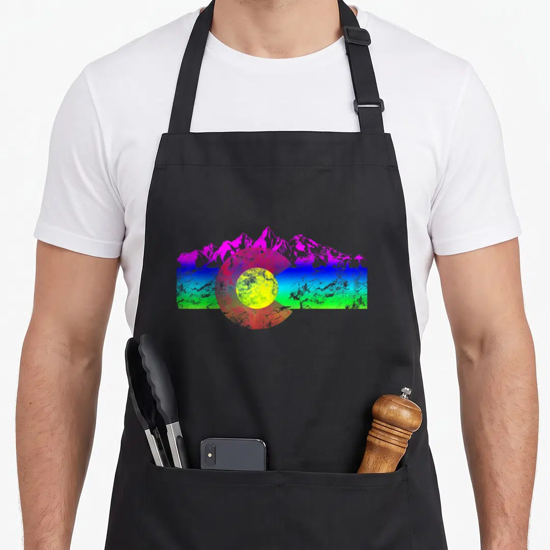 Mountain flag colorado apron - Retro letter C over gradient bar with pink mountains and yellow sun — shown on a black cotton canvas apron against a white background