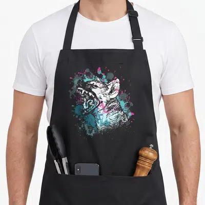Funny hyena apron - Cartoon dog head sketch surrounded by pink cyan grey and white paint splatters on black fabric — shown on a black cotton canvas apron against a white background