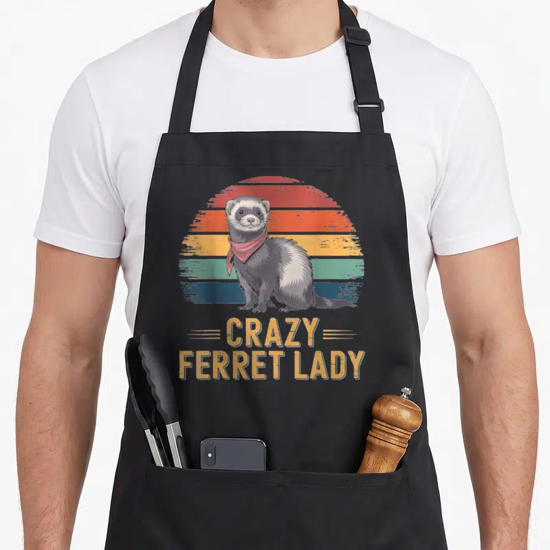Vintage ferret animal apron - Retro ferret in red bandana before striped sun with stacked CRAZY FERRET LADY text — shown on a black cotton canvas apron against a white background