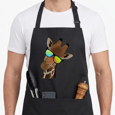 Zebras giraffe apron - Cartoon giraffe head wearing blue frame sunglasses with green and yellow lenses — shown on a black cotton canvas apron against a white background
