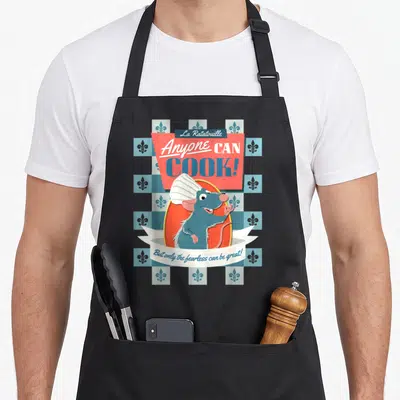 Poster remy ratatouille apron - Remy the rat in orange oval with Anyone Can Cook text on blue checkered background — shown on a black cotton canvas apron against a white background