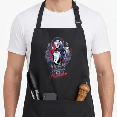 Suicide squad vehicle apron - Harley Quinn cartoon holding bat surrounded by red blue white diamonds and script text — shown on a black cotton canvas apron against a white background