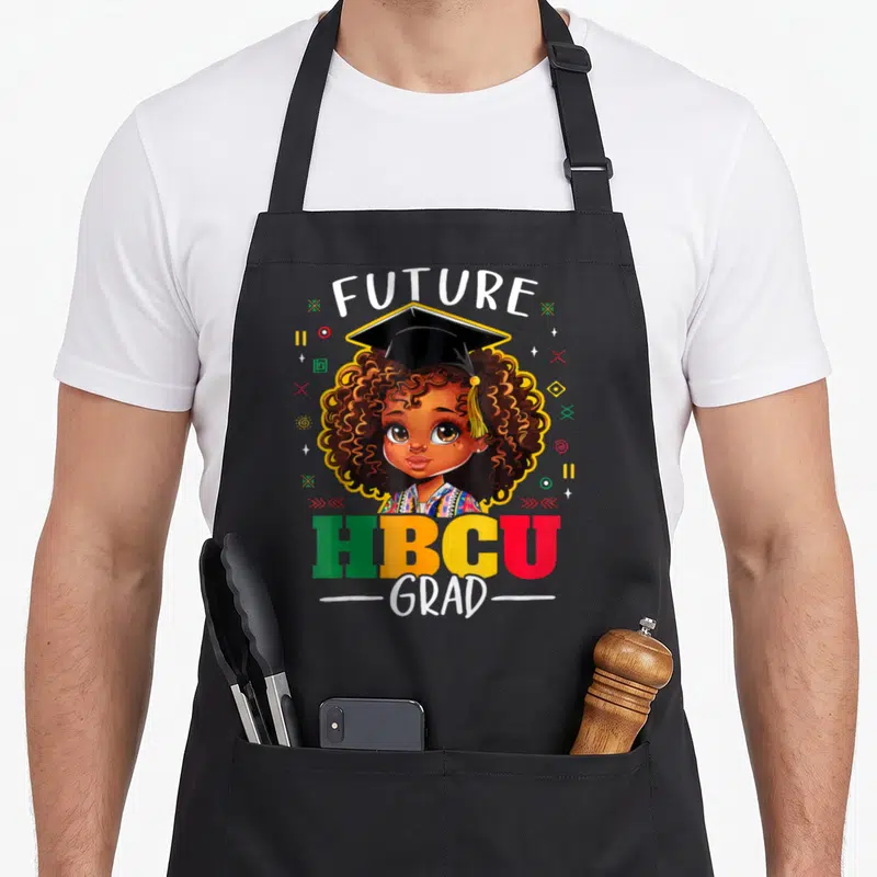 History motivational grade apron - Cartoon girl with afro wearing grad cap surrounded by FUTURE HBCU GRAD text — shown on a black cotton canvas apron against a white background
