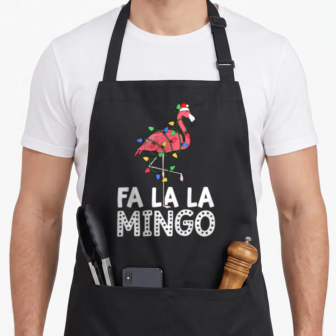 Mingo christmas tree apron - Pink flamingo in santa hat wrapped in multicolor lights above fa la la mingo text — shown on a black cotton canvas apron against a white background