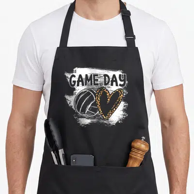 Volleyball game leopard apron - GAME DAY text above volleyball and leopard heart on distressed white background — shown on a black cotton canvas apron against a white background