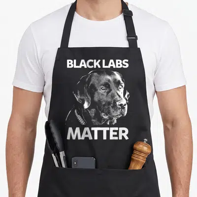 Matter labrador apron - White distressed black lab head graphic with BLACK LABS MATTER text — shown on a black cotton canvas apron against a white background