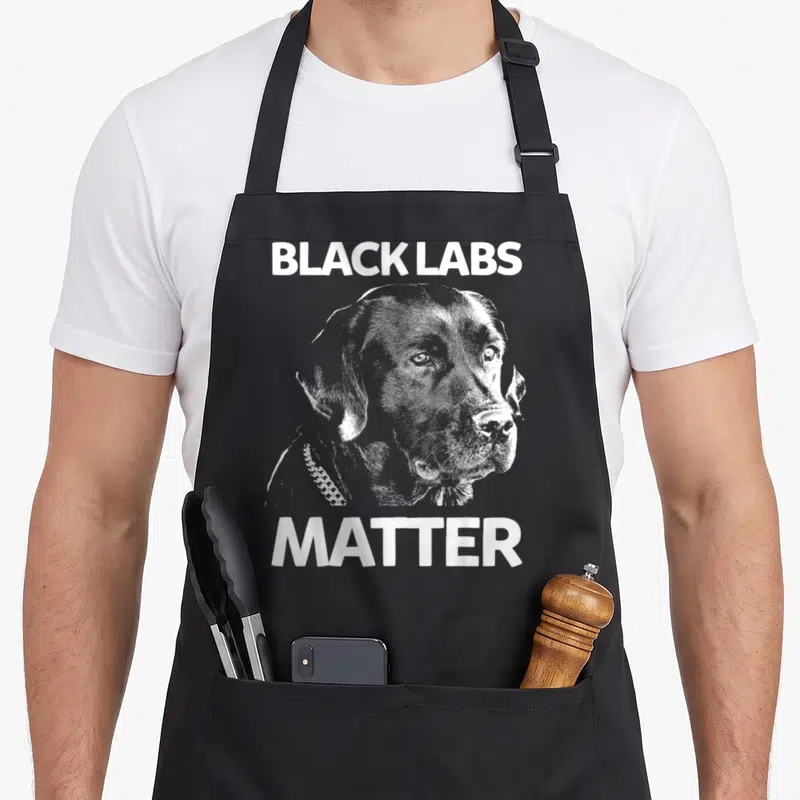 Matter labrador apron - White distressed black lab head graphic with BLACK LABS MATTER text — shown on a black cotton canvas apron against a white background